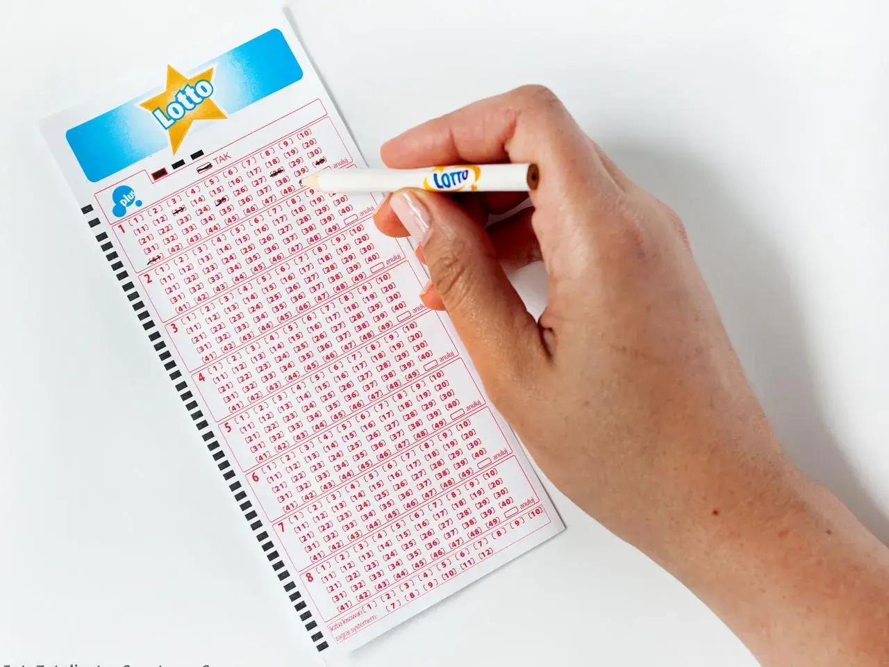 Dłoń z ołówkiem zaznacza liczby na kuponie Lotto. Zastanawiasz się, lotto ile jest do wygrania?
