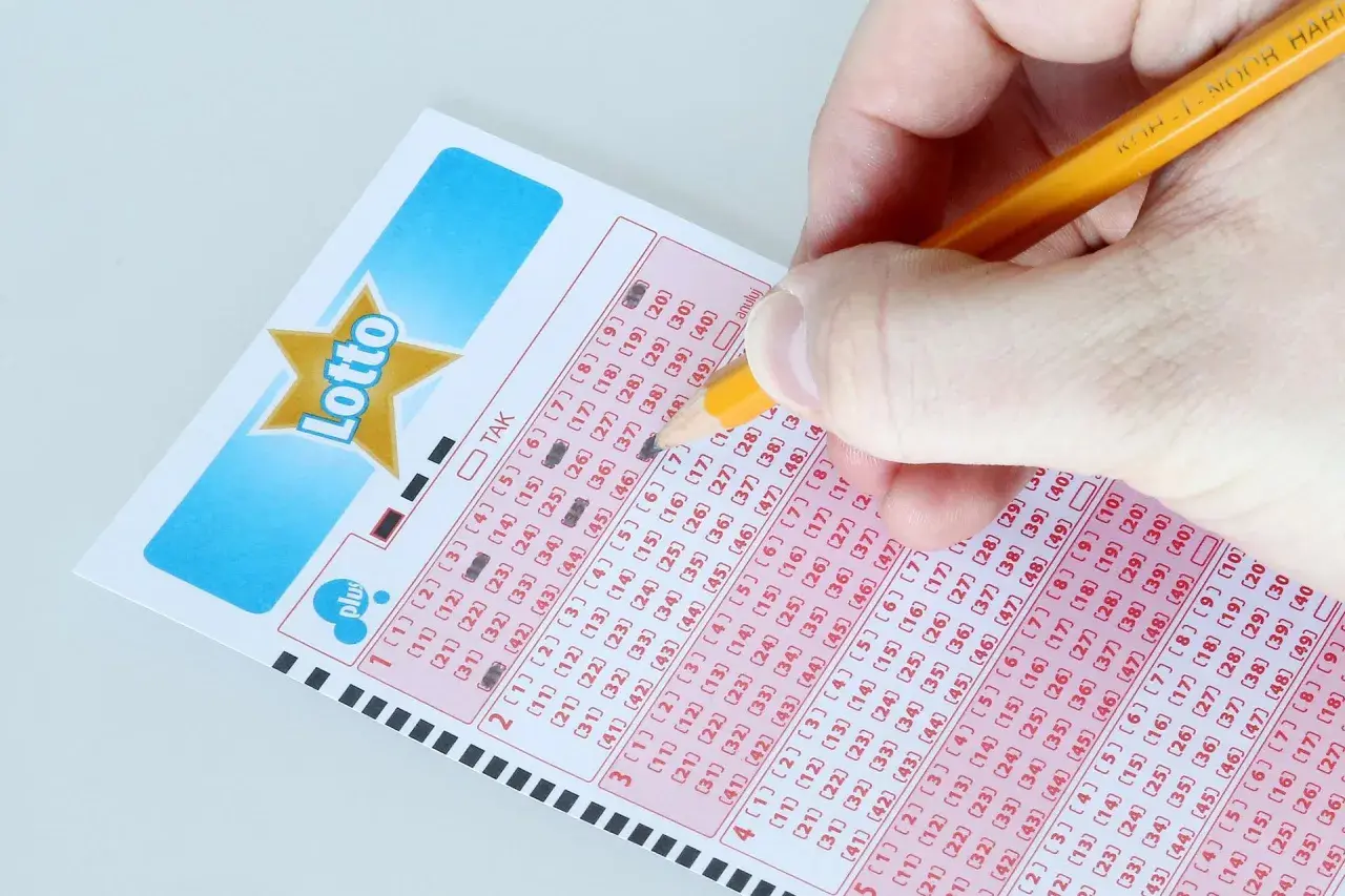 Ręka zaznacza liczby na kuponie Lotto, marząc o jackpot kiedy losowanie.