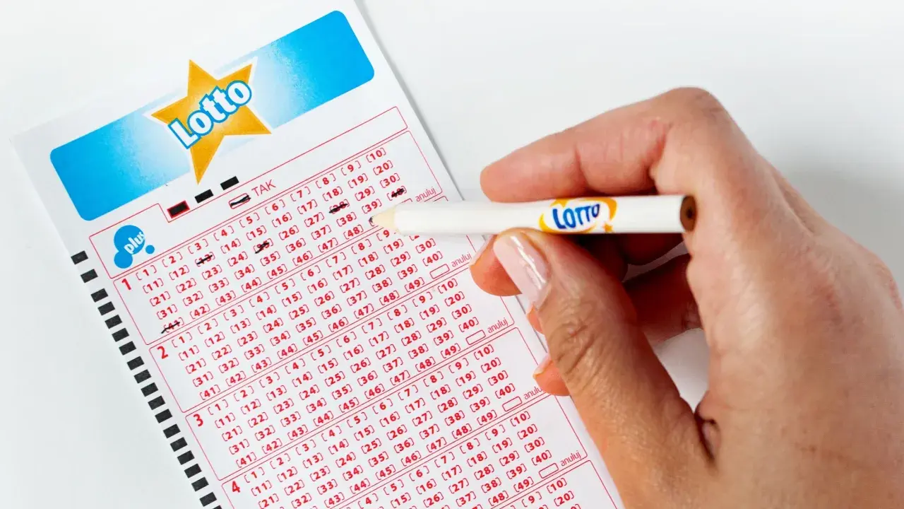 Dłoń z ołówkiem z logo Lotto zaznacza liczby na kuponie. Pytanie brzmi: jak długo ważny jest kupon lotto?