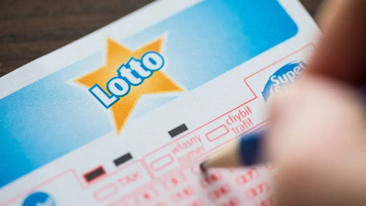 Ręka zaznacza liczby na kuponie Lotto. Planujesz grać w lotto w grupie? Dowiedz się, jak sporządzić umowę syndykatu.