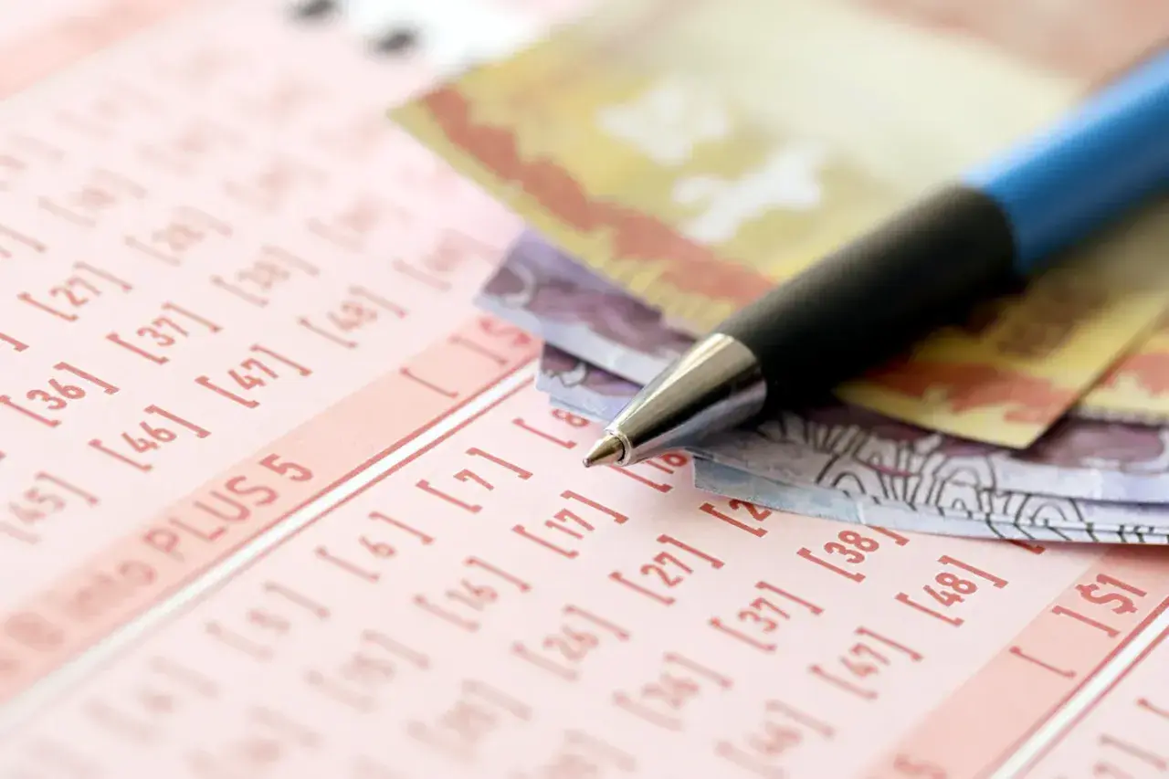 Długopis i banknoty na kuponie lotto. Dowiedz się, jak zorganizować loterię promocyjną w firmie zgodnie z prawem.