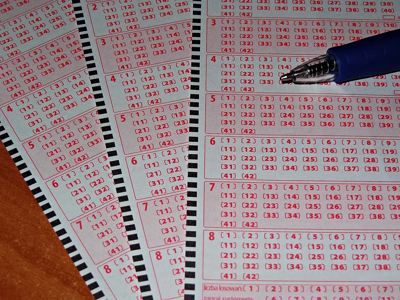 Zdrapki lotto z polami do zaznaczenia liczb i długopisem.