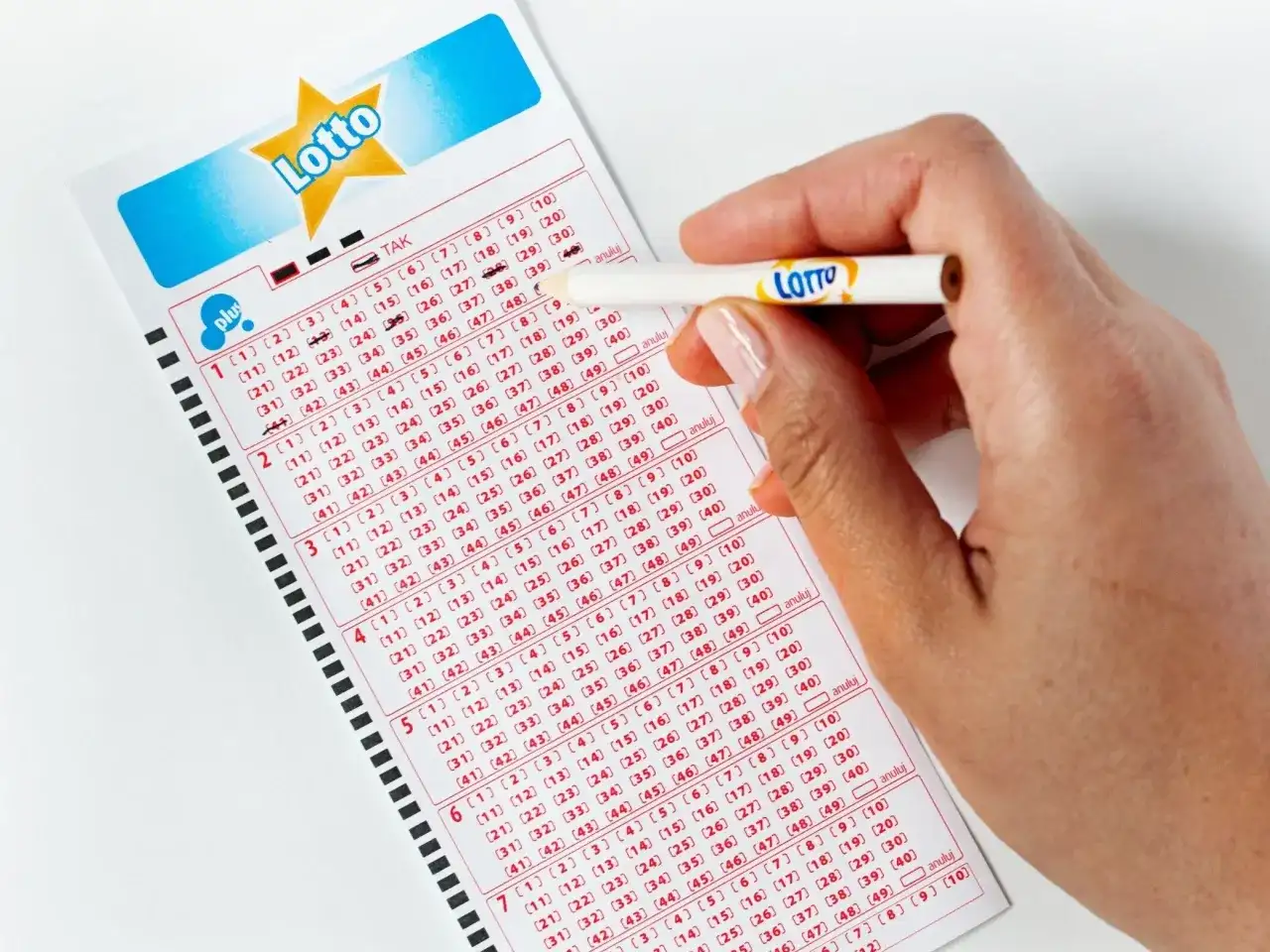 Ręka zaznacza liczby na kuponie Lotto. Aplikacja Lotto oferuje zniżki i promocje, pomagając łowić okazje.