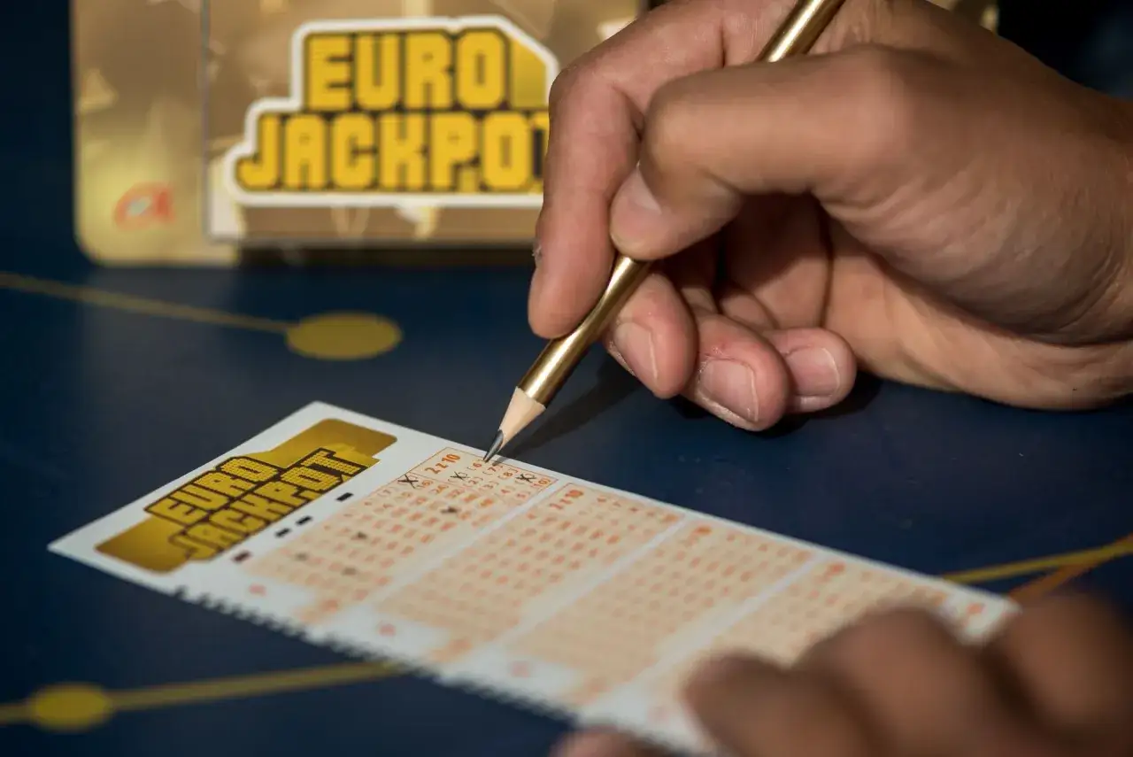 Dłoń z ołówkiem zaznacza liczby na kuponie loterii świątecznej Eurojackpot.