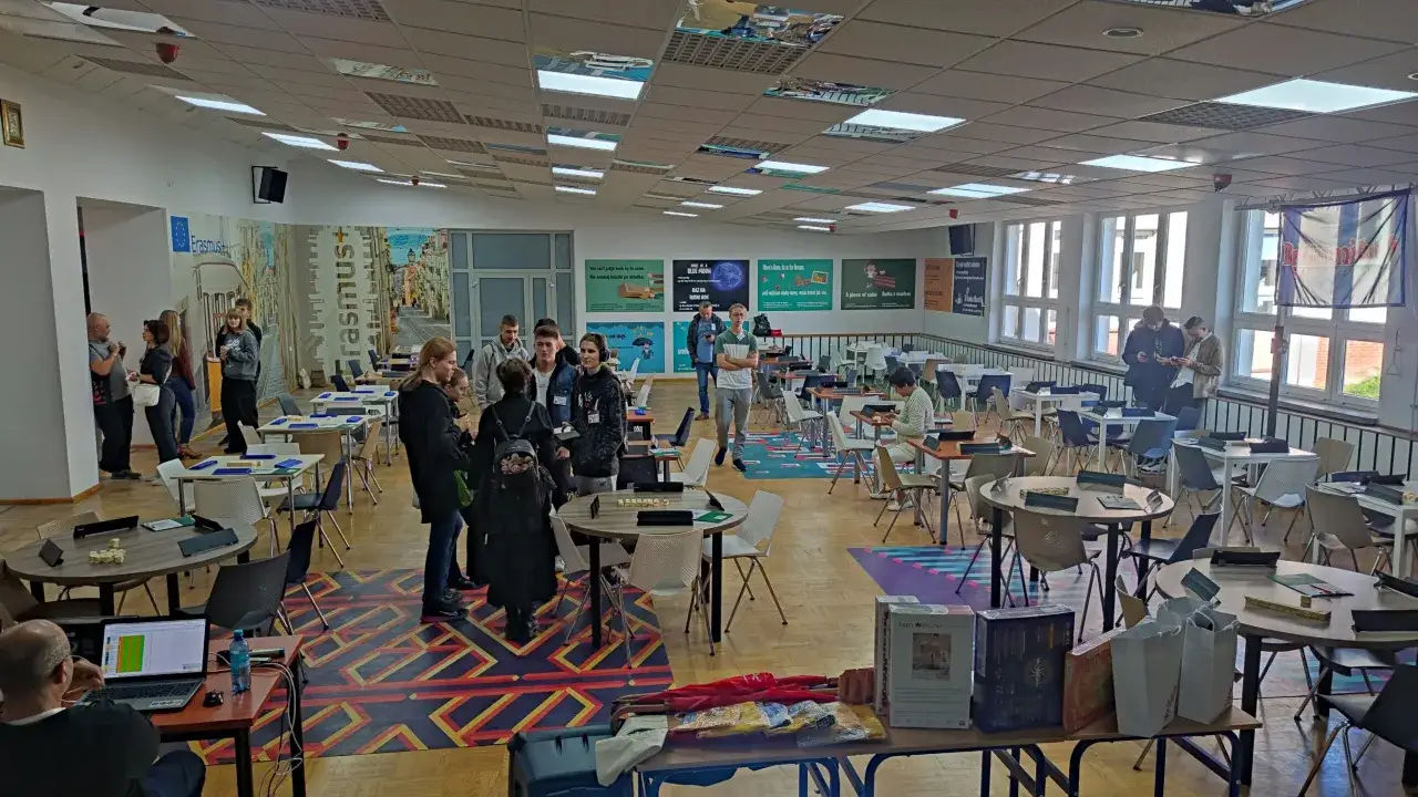 Uczestnicy turnieju podczas mistrzostw polski w rozwiązywaniu krzyżówek. Widać stoły z planszami i zawodników skupionych na grze.