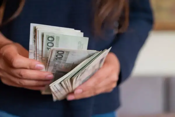 Ręce liczą banknoty 100 zł. Wygrana na zdrapce to darowizna, którą trzeba zgłosić do urzędu skarbowego.