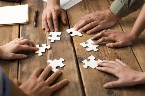 Dłonie składają puzzle, symbolizując wpływ codziennego rozwiązywania szarad na wydajność w pracy biurowej.