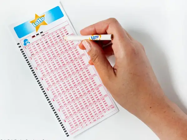 Dłoń z ołówkiem zaznacza liczby na kuponie Lotto. Zastanawiasz się, lotto ile jest do wygrania?