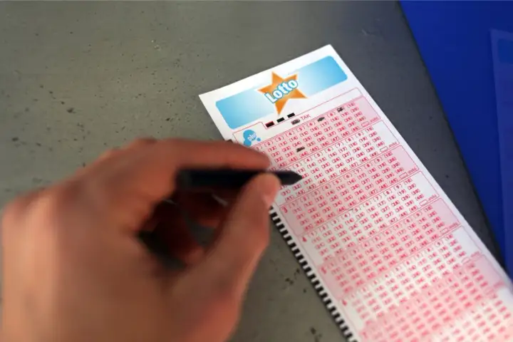 Ręka zaznacza liczby na kuponie Lotto. Analiza historycznych wyników pod kątem najrzadziej padających liczb.